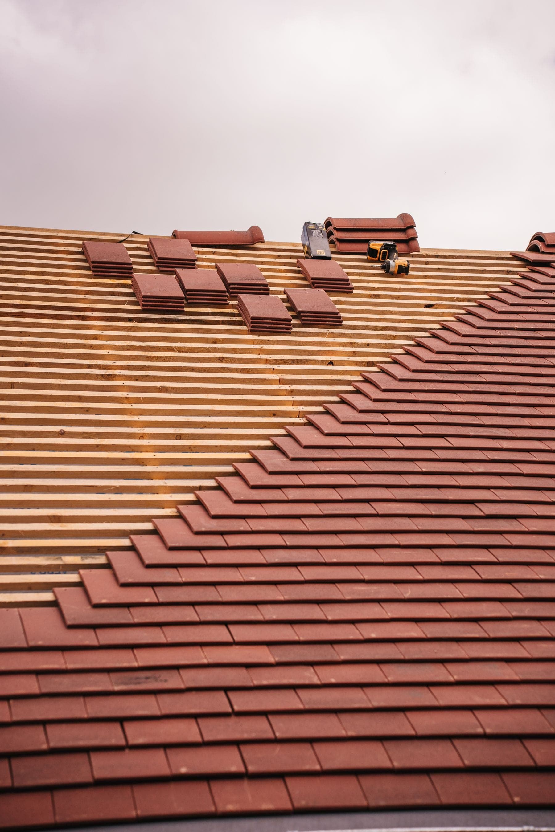 Red clay plain tiles being laid on new battens on a pitched roof